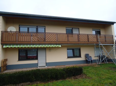 Zweistöckiges Wohnhaus mit Balkon und einer Leiter im Garten.