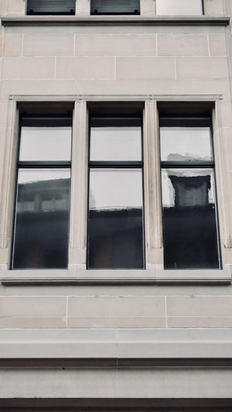 Drei gleich große Fenster mit schmalen Rahmen in einer hellen Gebäudefassade.