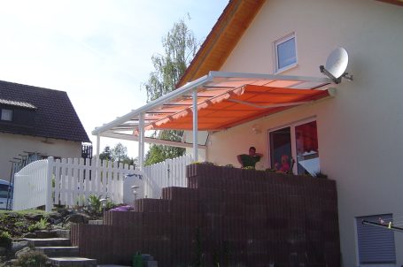 Haus mit oranger Markise und Eingangstreppe in einem Gartenbereich.