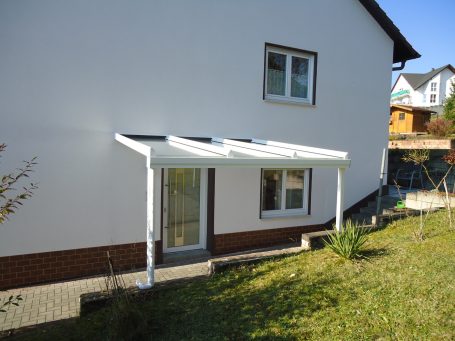 Weißes Haus mit überdachter Terrasse und Garten.