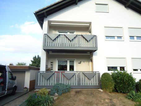 Balkon eines Hauses mit grauen Geländern und Sichtschutz, umgeben von Pflanzen.