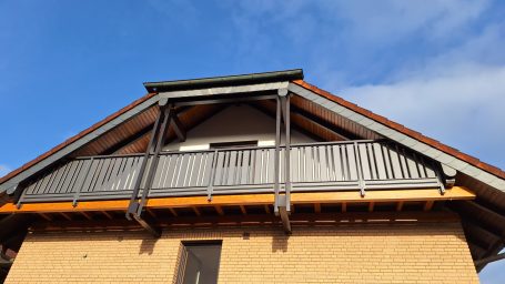 Dach mit Balkon und Holzverkleidung unter klarem blauen Himmel.