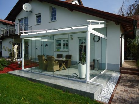 Modernes Haus mit verglastem Wintergarten und Terrassenmöbeln.