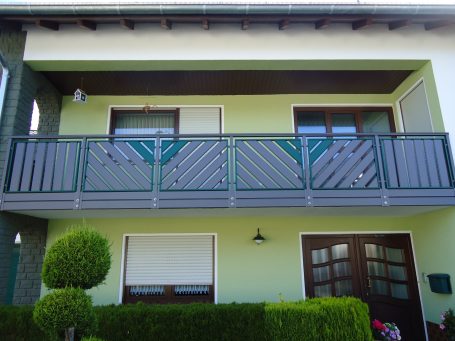 Fassade eines Hauses mit Balkon und grün gestrichenen Wänden, umgeben von Sträuchern.