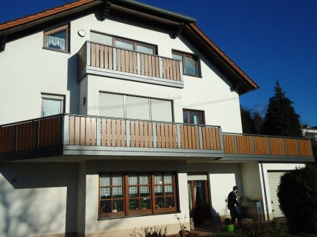 Modernes Haus mit Holzverkleidung, Balkon und großen Fenstern vor klarem, blauem Himmel.
