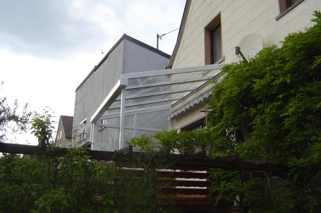 Terrasse mit Überdachung und angrenzendem Wohnhaus, umgeben von Pflanzen.