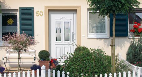 Eingang zu einem gepflegten Haus mit Garten und einer weißen Zaunreihe.