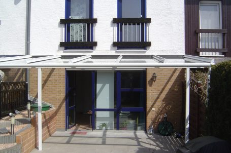 Eingang zu einem Gebäude mit einer weißen Überdachung und blauen Fenstern.