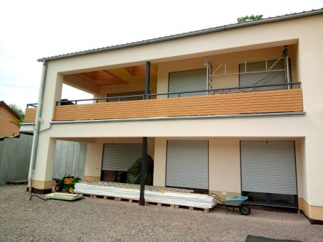 Modernes zweigeschossiges Haus mit Balkon, Rolläden und gepflastertem Hof.
