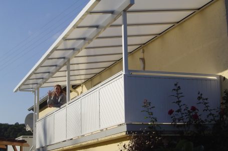 Balkon mit Überdachung und Pflanzen, eine Person sitzt entspannt darauf.