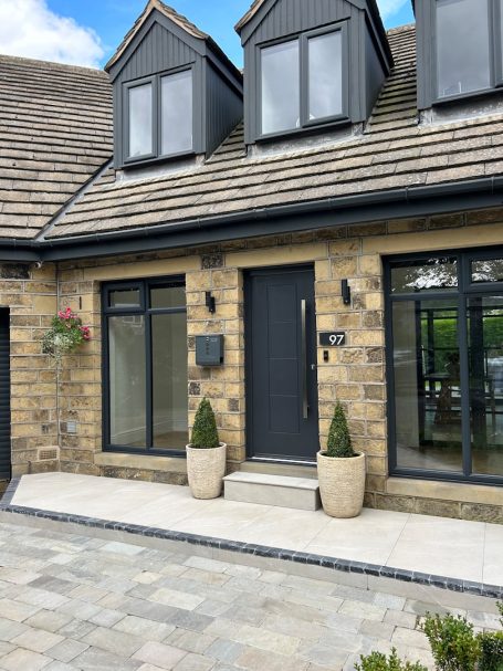 Eingang zu einem modern gestalteten Haus mit blauen Fenstern und zwei Pflanzenkübeln.