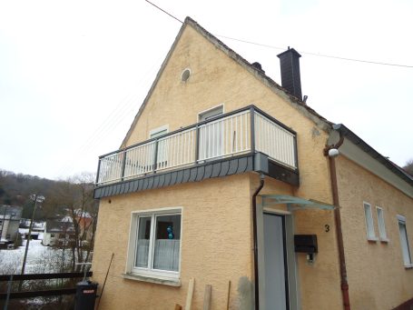 Gelbes Haus mit Balkon und schneebedecktem Boden im Hintergrund.
