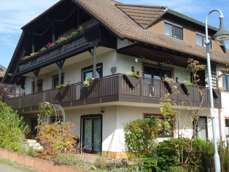 Mehrstöckiges Haus mit Balkon, blühenden Pflanzen und ruhiger Umgebung.