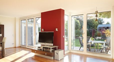 Heller Wohnraum mit roter Wand, Fernseher und Blick auf den Garten.