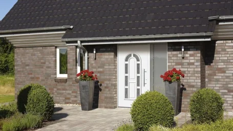 Eingang zu einem modernen Haus mit blühenden Pflanzen und symmetrischen Topfpflanzen.