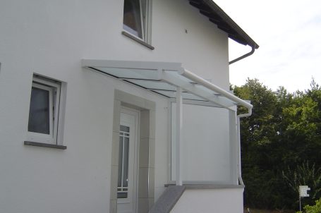 Vordach über einer Haustür mit gläserner Überdachung und hellem Rahmen.