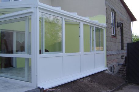 Veranda mit weißen Rahmen, angelehnt an ein graues Steinhaus, grüner Innenanstrich.