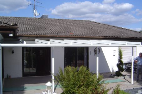 Haus mit überdachter Terrasse und Garten, unter einem blauen Himmel mit Wolken.